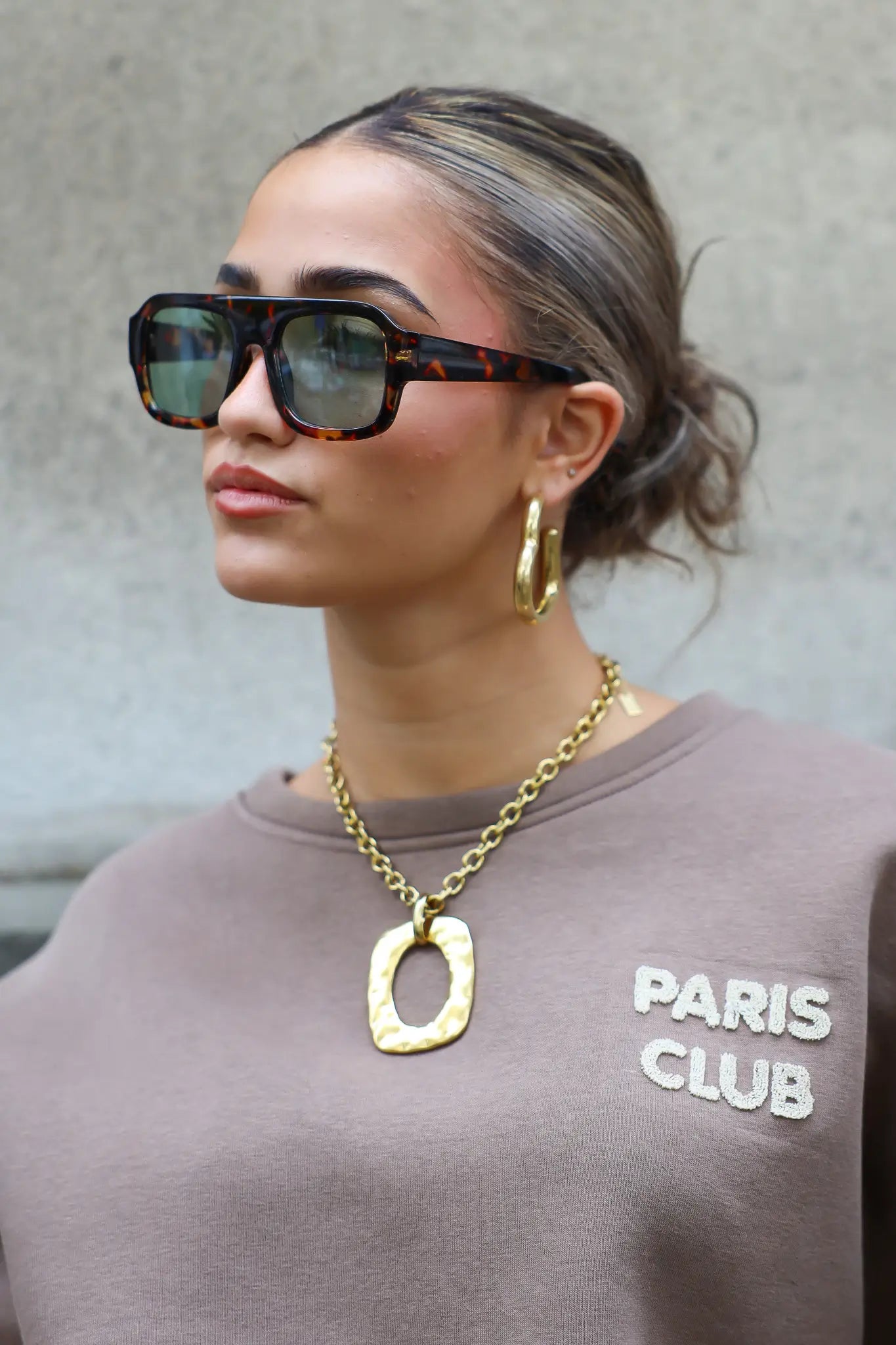 close-up van model met donkergroene zonnebril, gouden ketting en trui met Paris Club logo