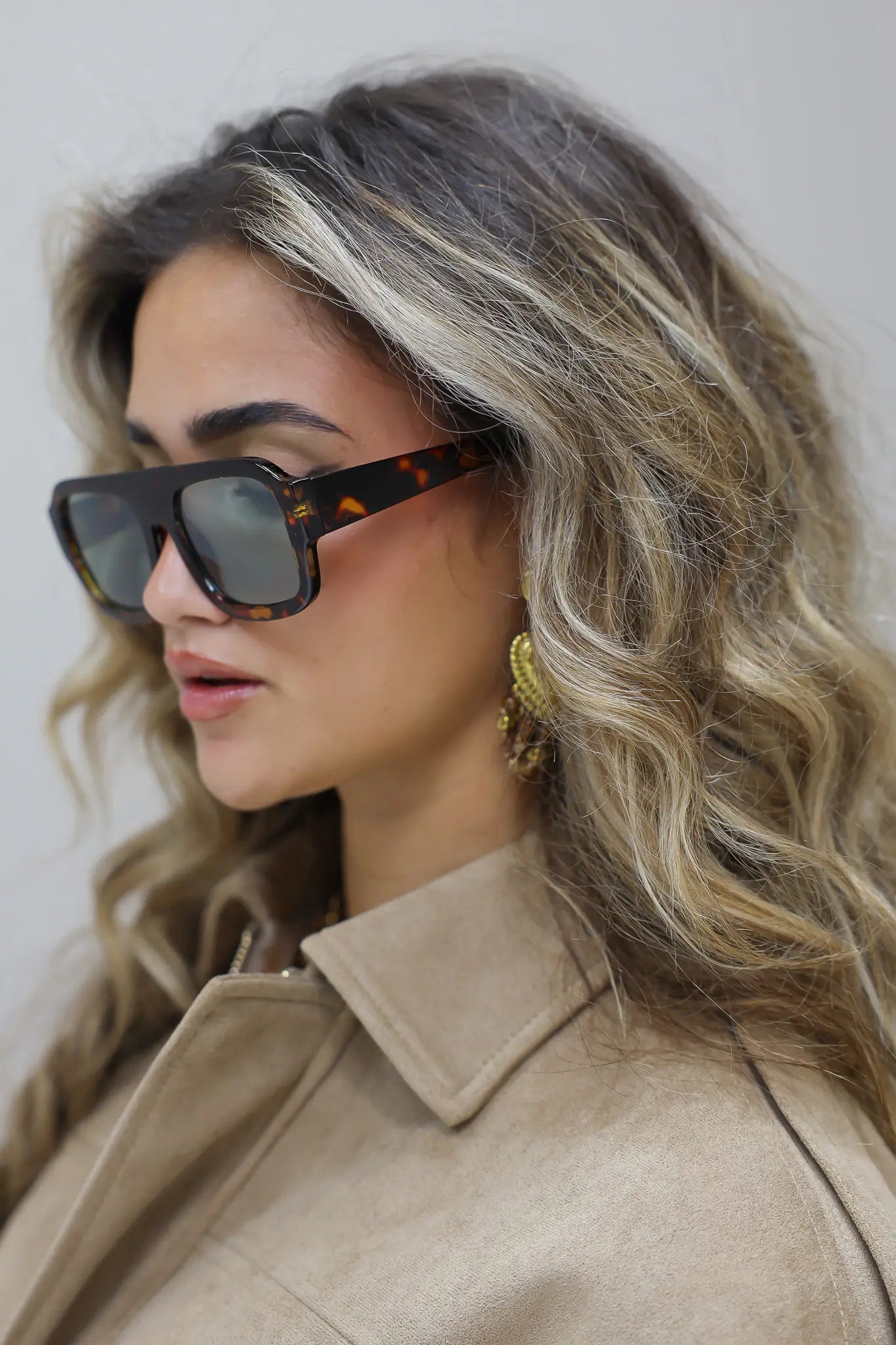 model met zonnebril kijkt opzij met los haar en beige blouse