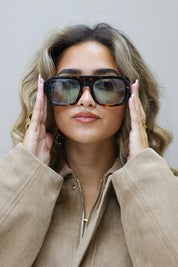 model met zonnebril houdt beide handen bij haar bril en kijkt recht vooruit