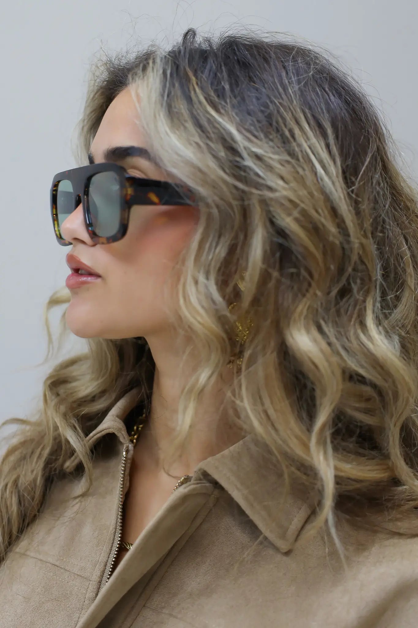 model met zonnebril kijkt schuin opzij, golvend haar over schouder