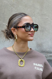 model met zonnebril kijkt opzij met opgestoken haar en gouden oorbellen