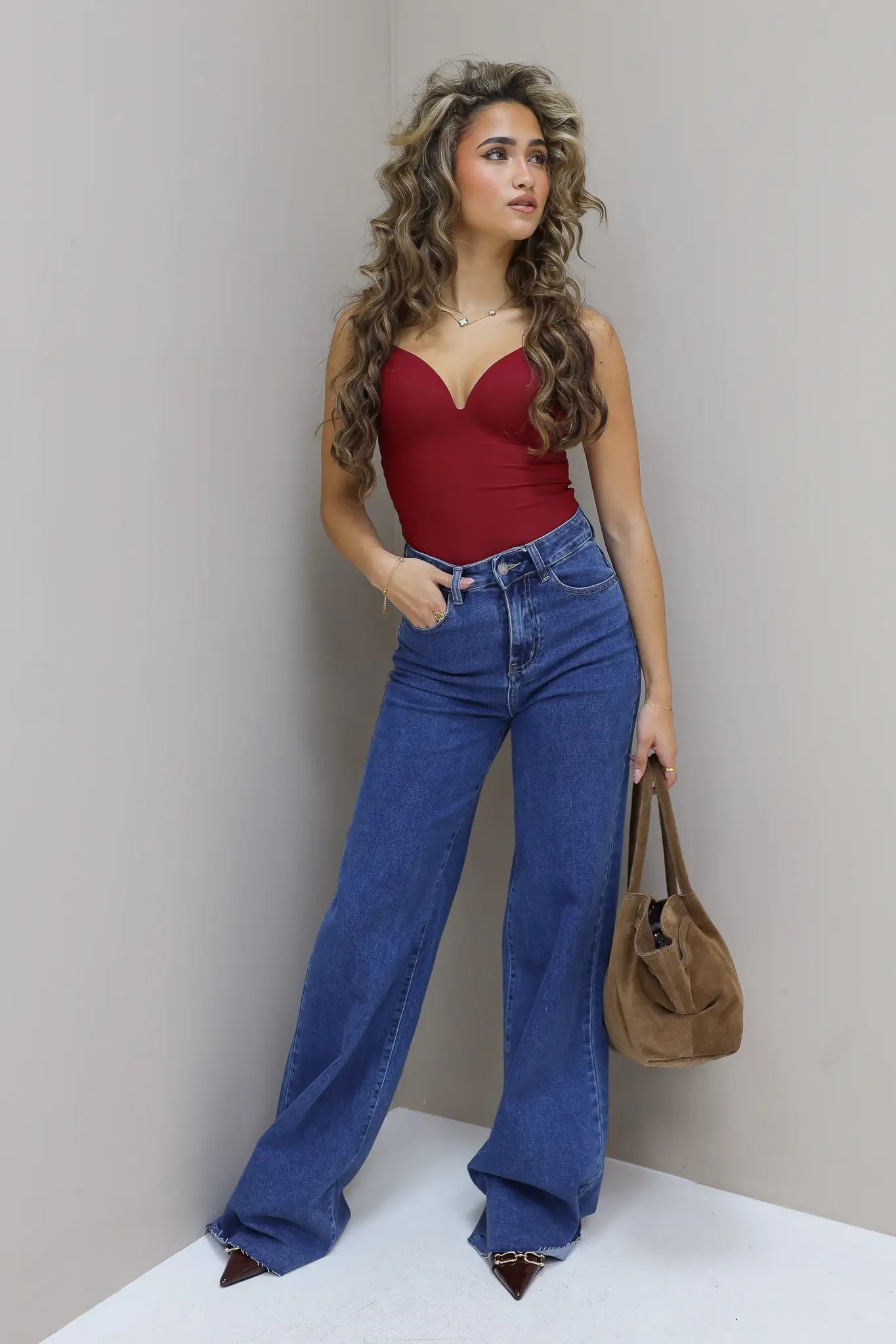 Model leunt licht tegen muur, jeans valt wijd over hakken