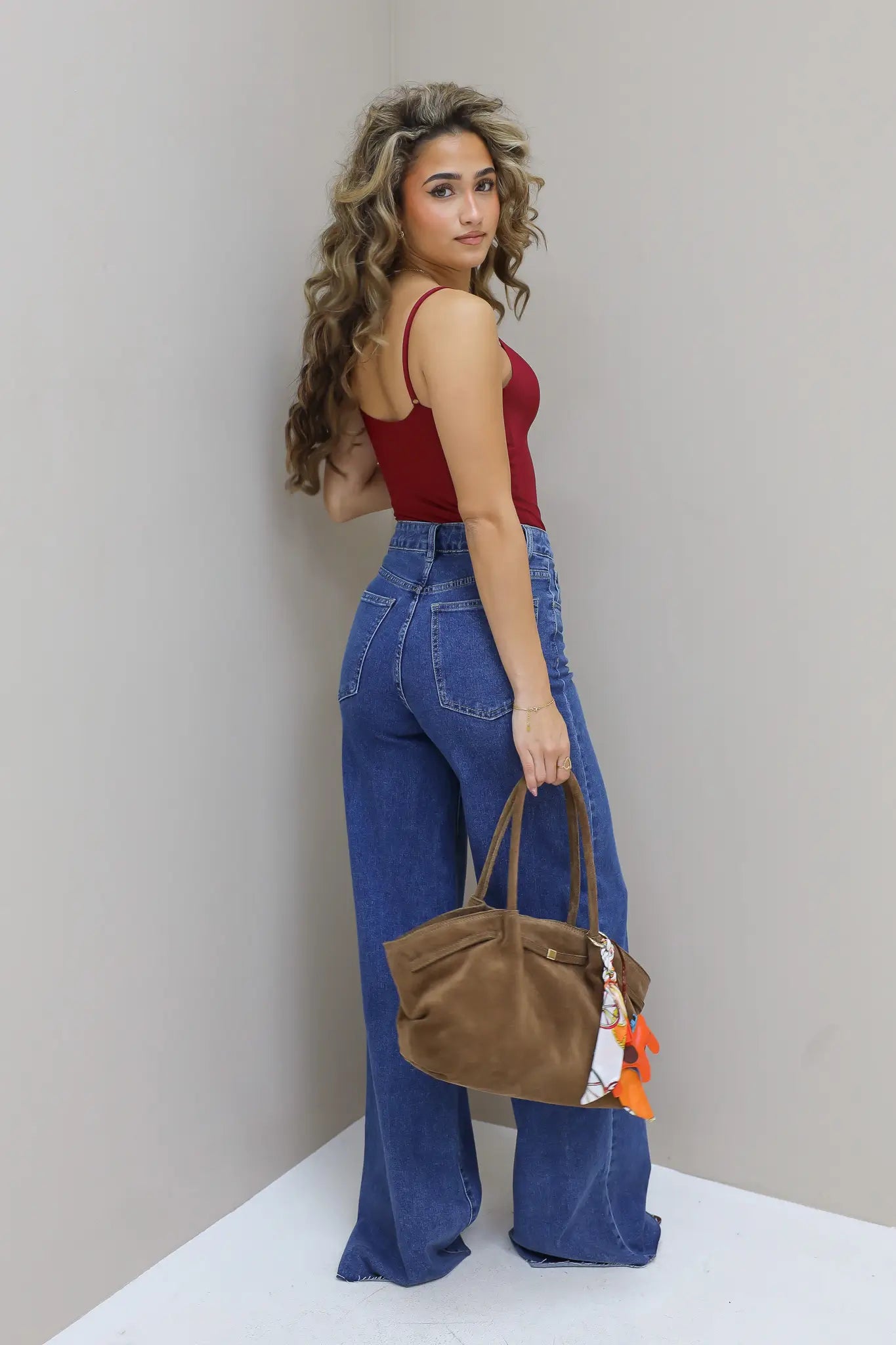Model toont de zijkant van de jeans met bruine tas in hand