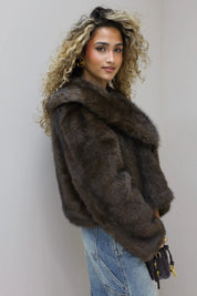 model staat zijwaarts met bruin faux fur jasje en handtas