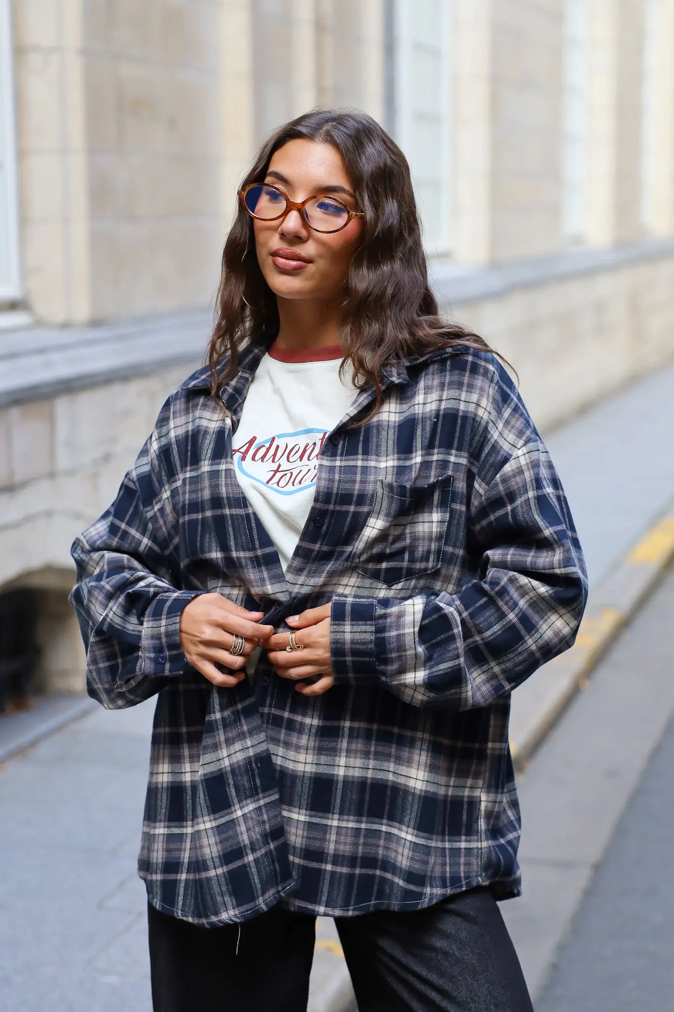 Model draagt een donkerblauwe geruite flanellen blouse met een oversized pasvorm, gecombineerd met een crème T-shirt en zwarte jeans.
