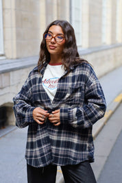 Model draagt een donkerblauwe geruite flanellen blouse met een oversized pasvorm, gecombineerd met een crème T-shirt en zwarte jeans.
