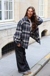 Zijaanzicht van een donkerblauwe oversized flanellen blouse met ruitpatroon en lange mouwen, gecombineerd met een zwarte jeans.
