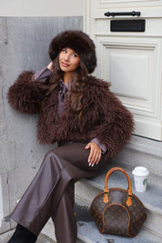 Model zit buiten met fluffy muts bruin, jas en tas