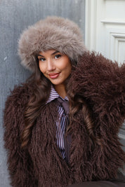 Close-up van model met taupe fluffy muts en bruine jas