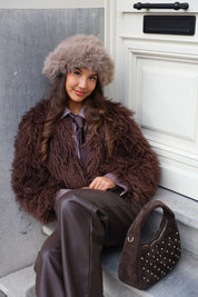 Model met taupe fluffy muts in zijaanzicht bij witte deur