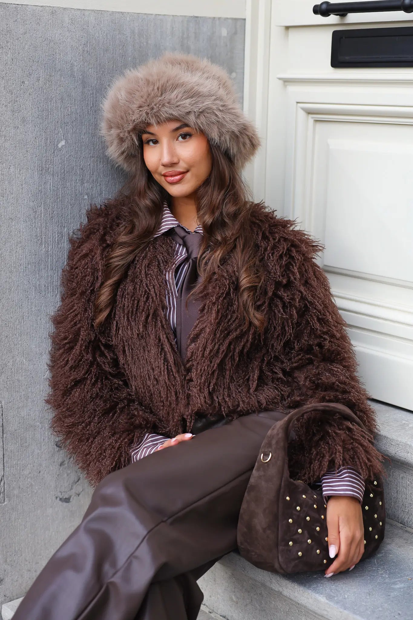 Model zit op trap met taupe fluffy muts en bruine jas