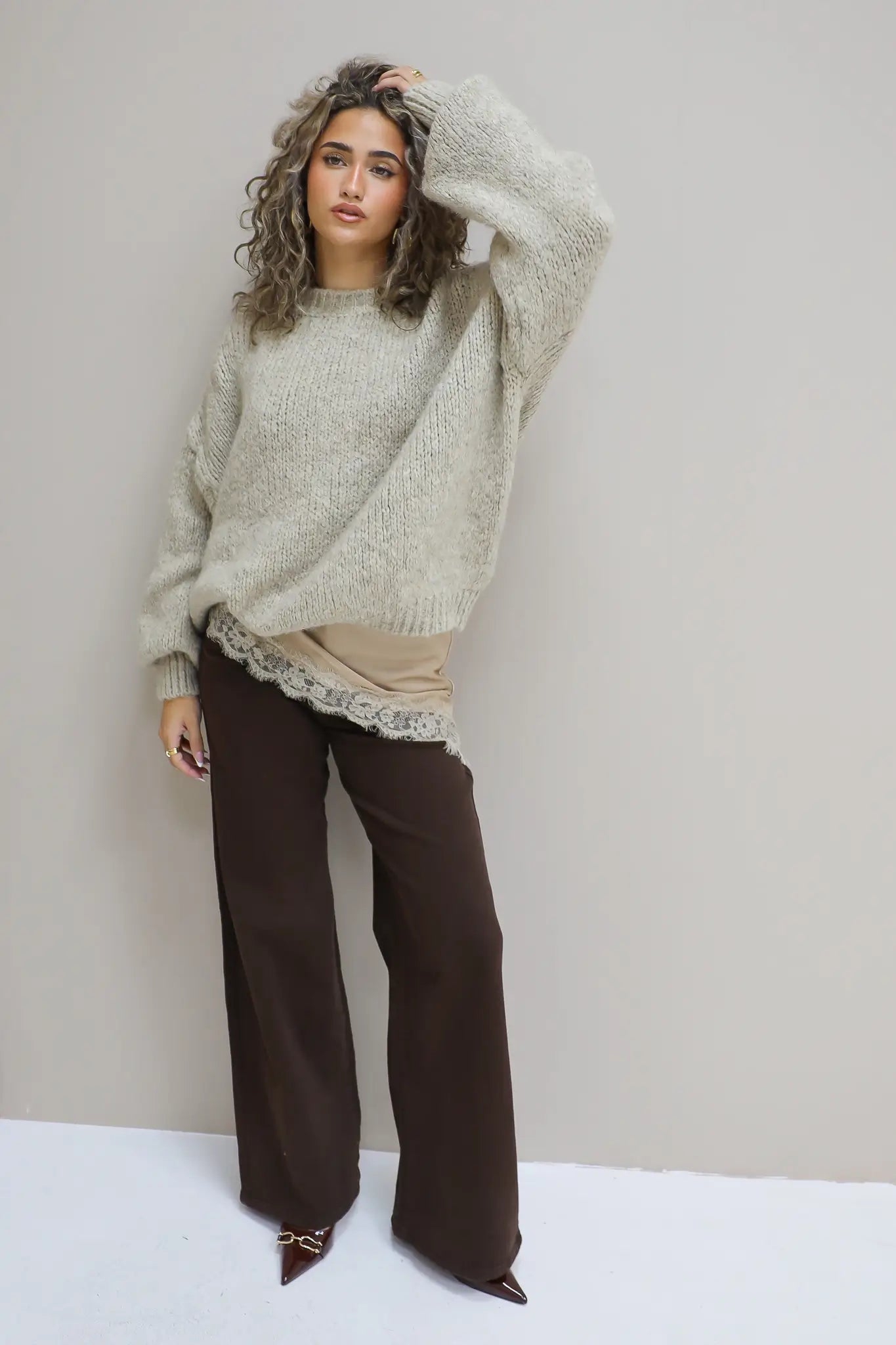 model draagt losvallende beige trui met bruine pantalon