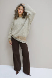 model draagt losvallende beige trui met bruine pantalon