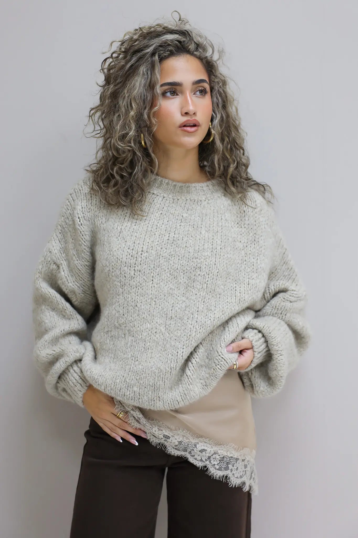 model draagt zachte beige trui over satijnen top met kant