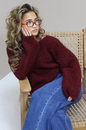 Model leunt met elleboog op stoel, nonchalante houding met bordeaux trui