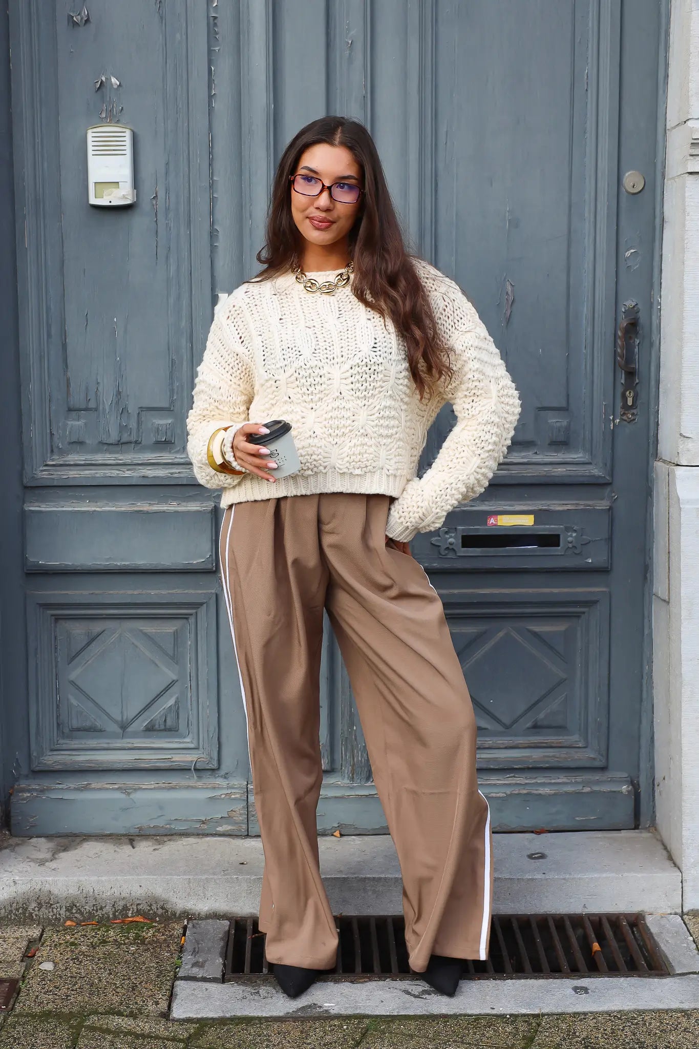 model draagt creme trui met bruine broek buiten bij blauwe deur