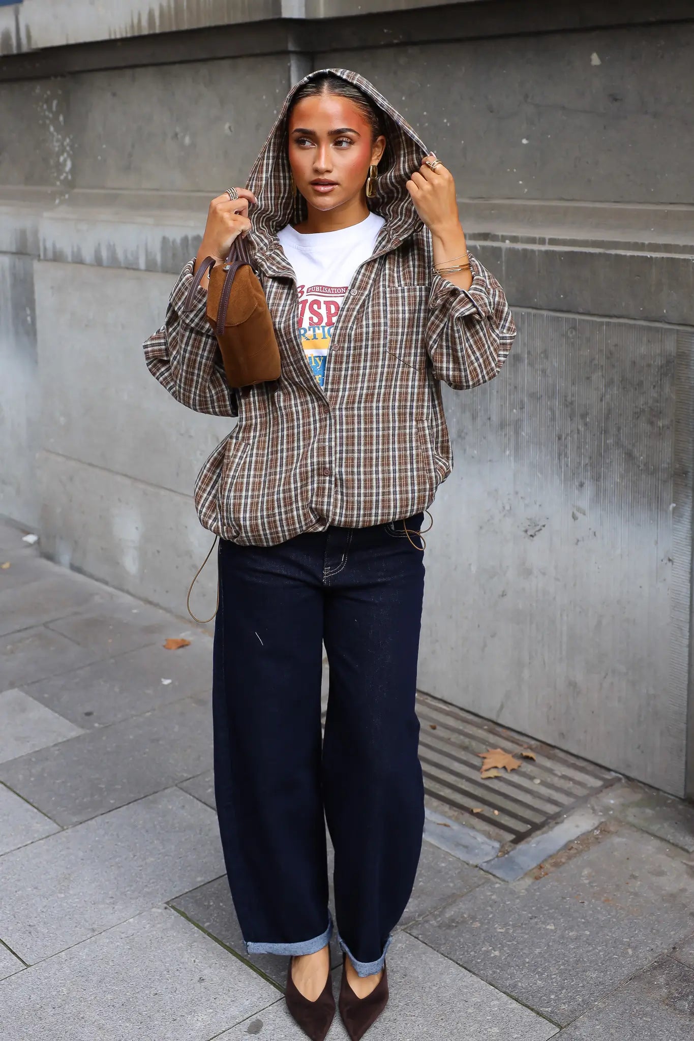 Geruite camel blouse met capuchon gedragen over een wit shirt met donkere wijde jeans en zwarte schoenen
