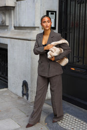 Taupe getailleerde blazer met dubbele knoopsluiting gecombineerd met een wijde pantalon en bonttas