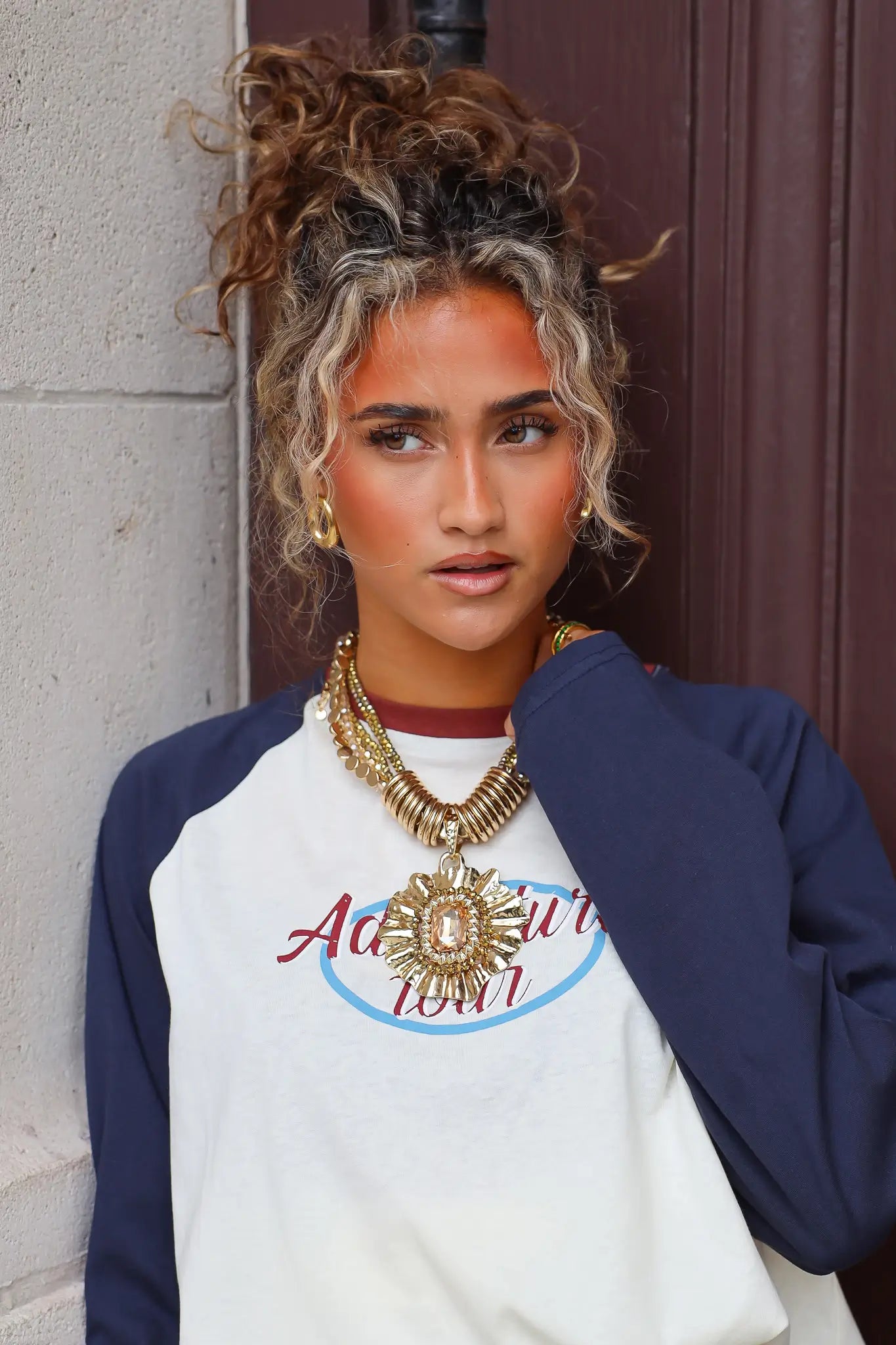 Gouden ketting met meerdere lagen en opvallende ronde hanger gedragen bij een casual shirt met print