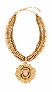 Gouden statement ketting met meerdere lagen schakels en kralen en een grote bloemvormige hanger op witte achtergrond
