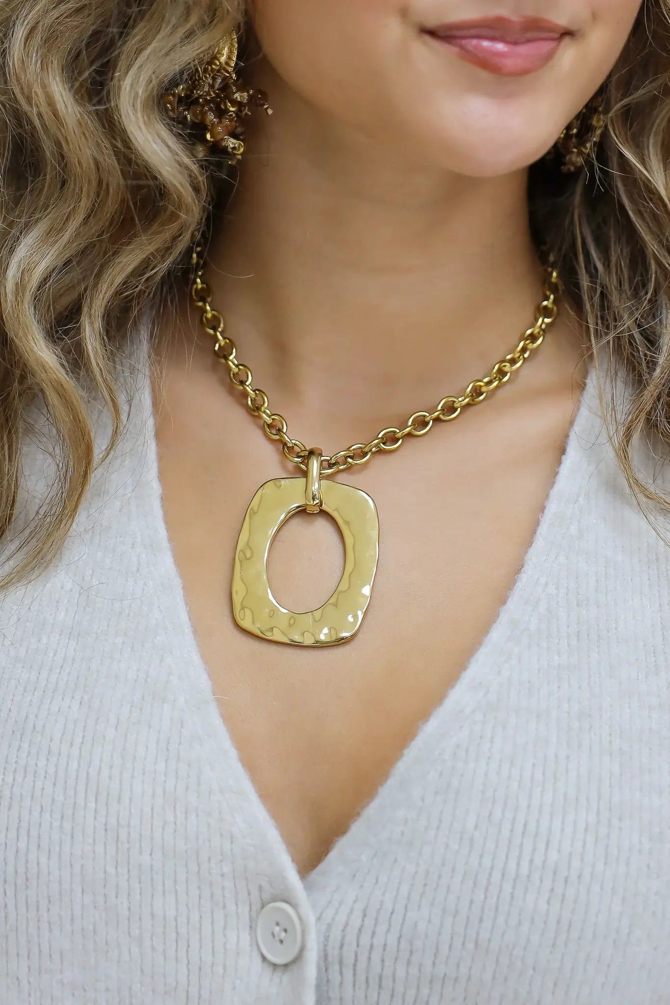 close-up van gouden ketting met grote ovale hanger gedragen bij wit vest