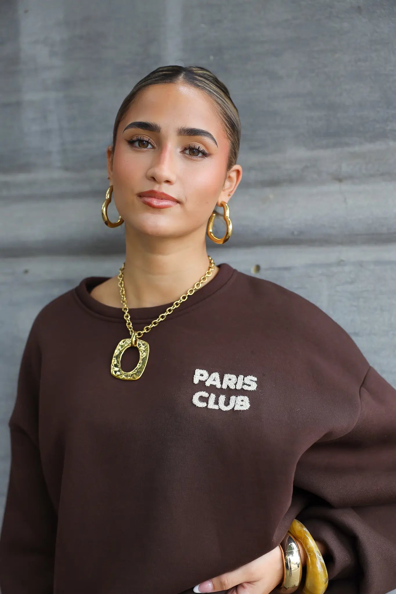 detailfoto van gouden ketting bij bruine trui, hanger zichtbaar op borst