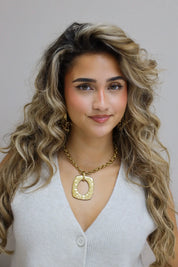 model draagt ketting met grote gouden hanger en glimlacht richting camera