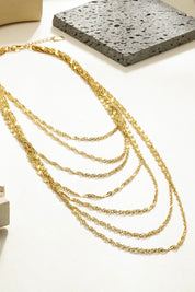 gouden kettingen in lagen weergegeven naast een siersteen en wit plateau