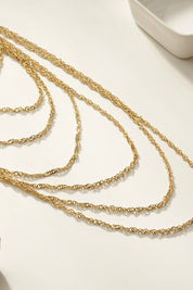 set van meerdere gouden kettingen in verschillende lengtes plat neergelegd op witte ondergrond