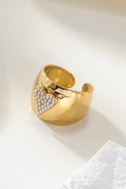 gouden ring met ingelegd hart van steentjes gefotografeerd op witte stof en zachte belichting
