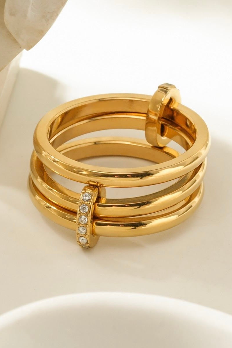 close-up van gouden ring met meerdere banden en ingelegde steentjes op witte achtergrond