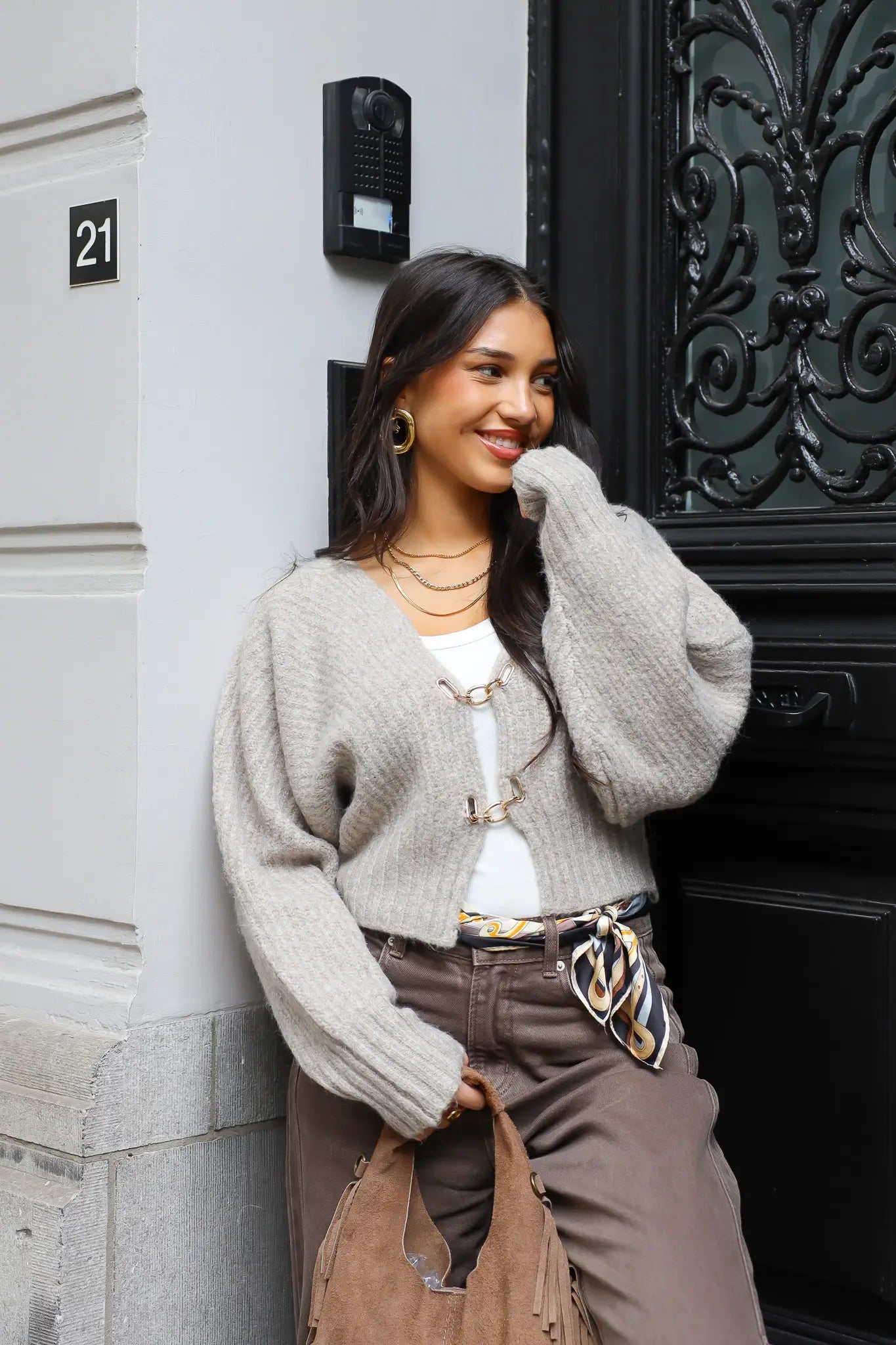 Model draagt een grijs gebreid vest bij een zwarte voordeur