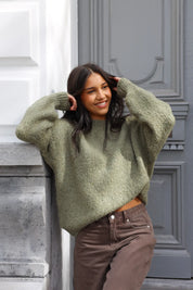 Model leunt tegen muur in groene fluffy trui met bruine broek