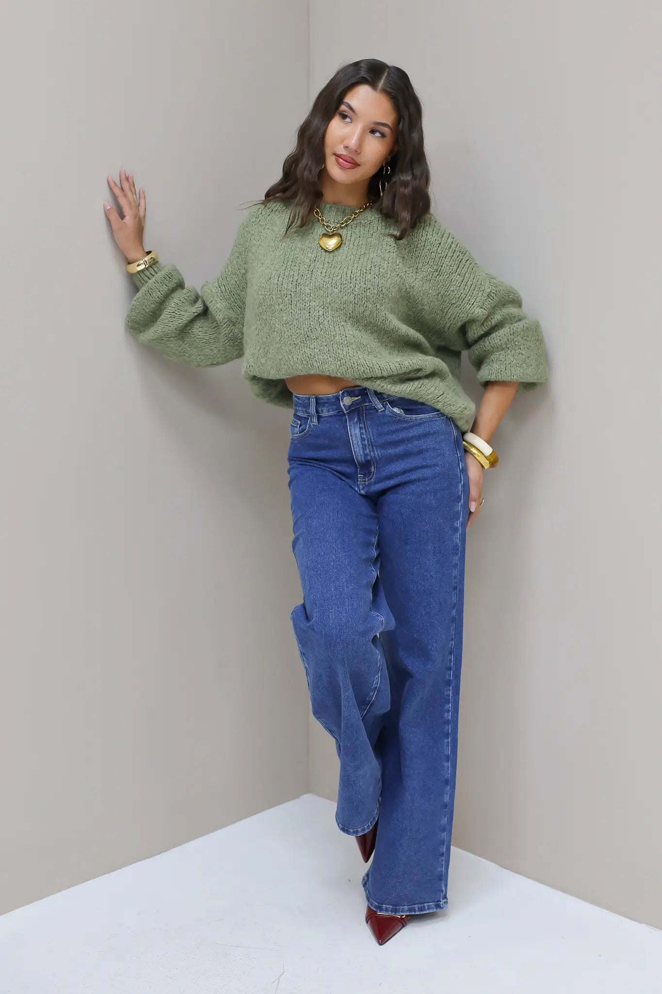 Model staat in groene fluffy trui met blauwe jeans en gouden accessoires