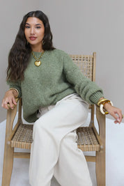 Model zit ontspannen op stoel in groene fluffy trui met witte broek