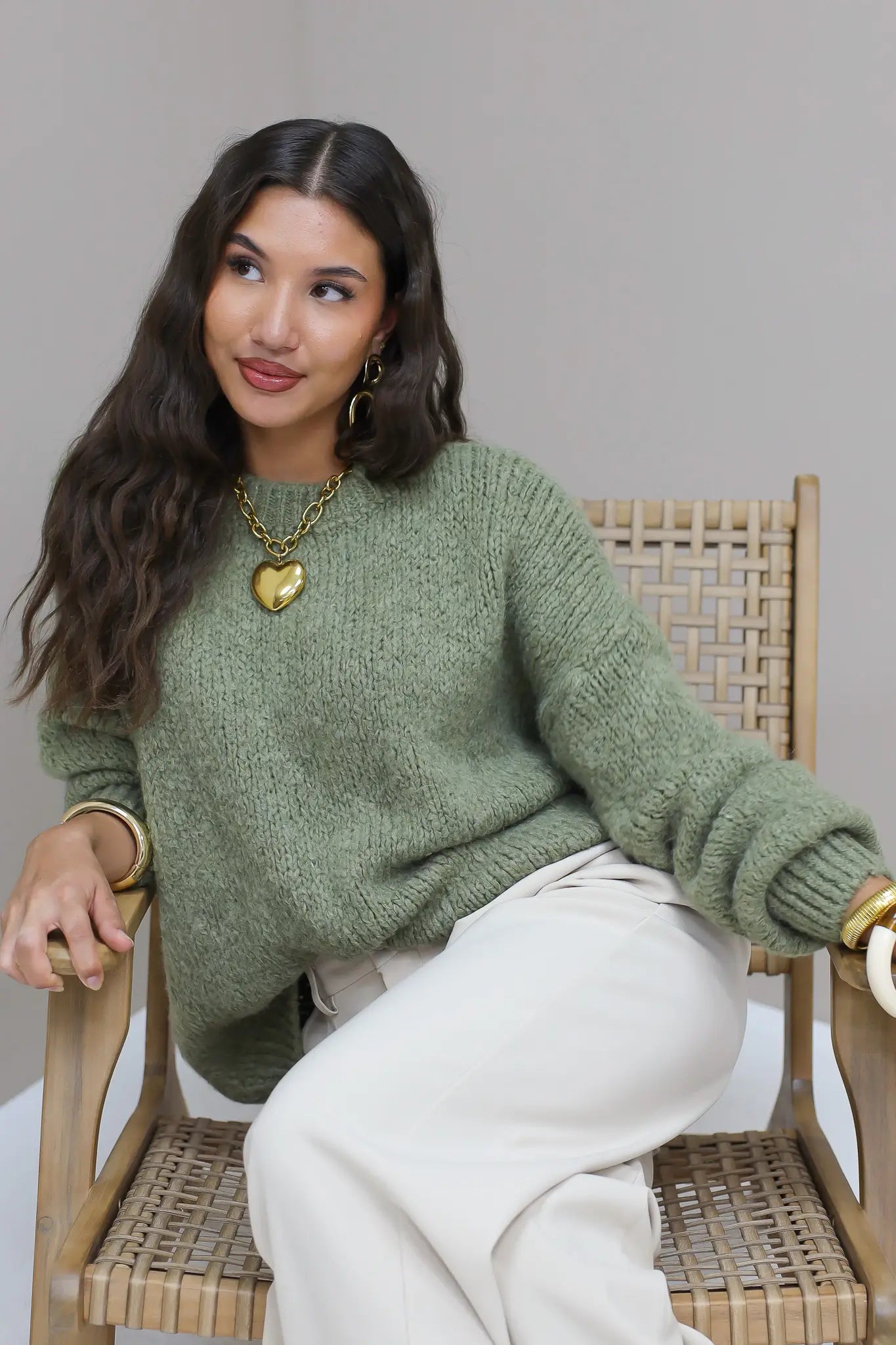 Model zit op houten stoel in groene fluffy trui met witte broek