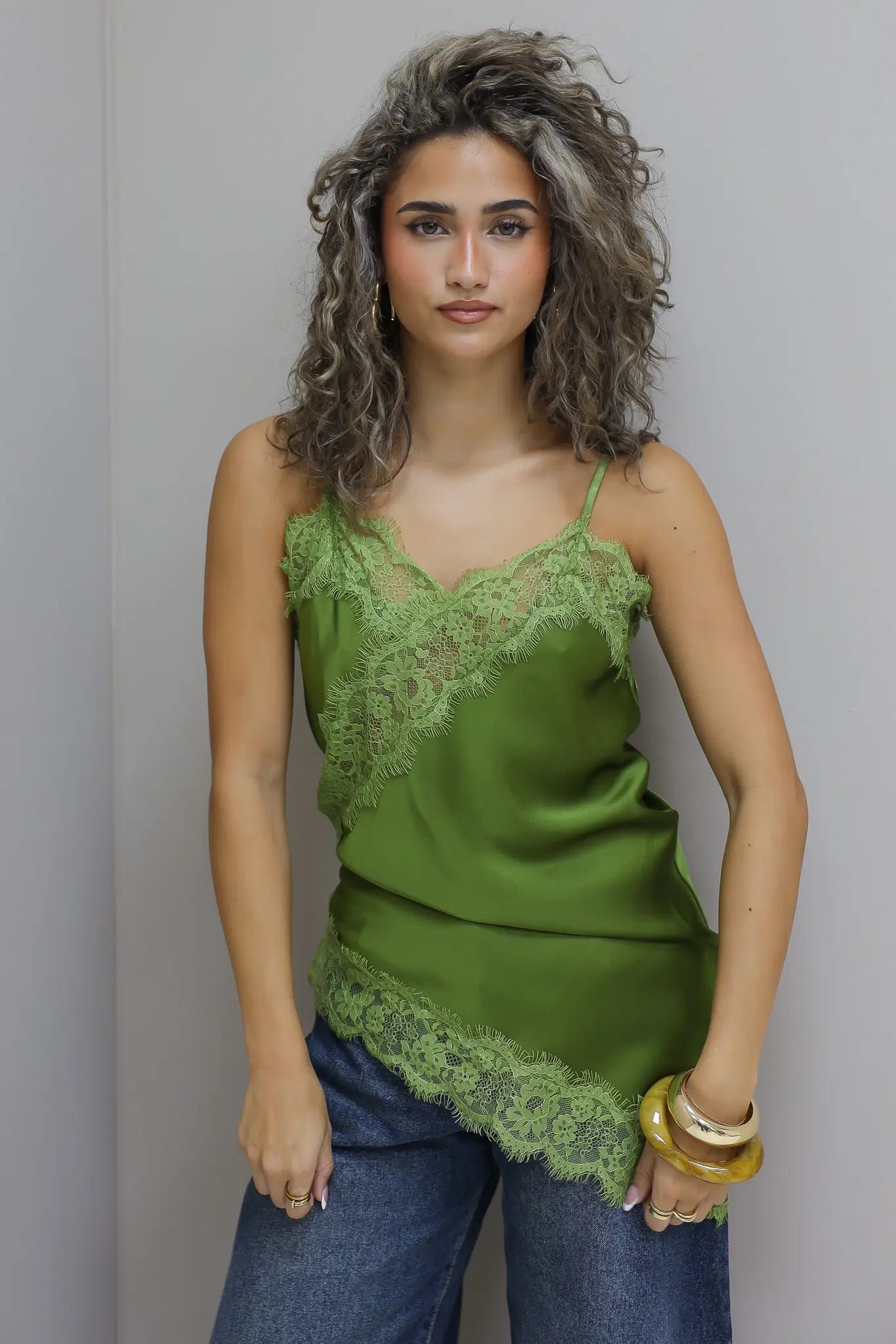 model draagt groene satijnen top met kanten rand en jeans