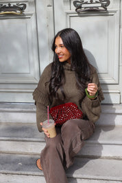 Model zit buiten tegen een deur met groene trui