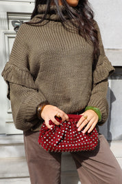 Model staat buiten met groene trui en rode tas