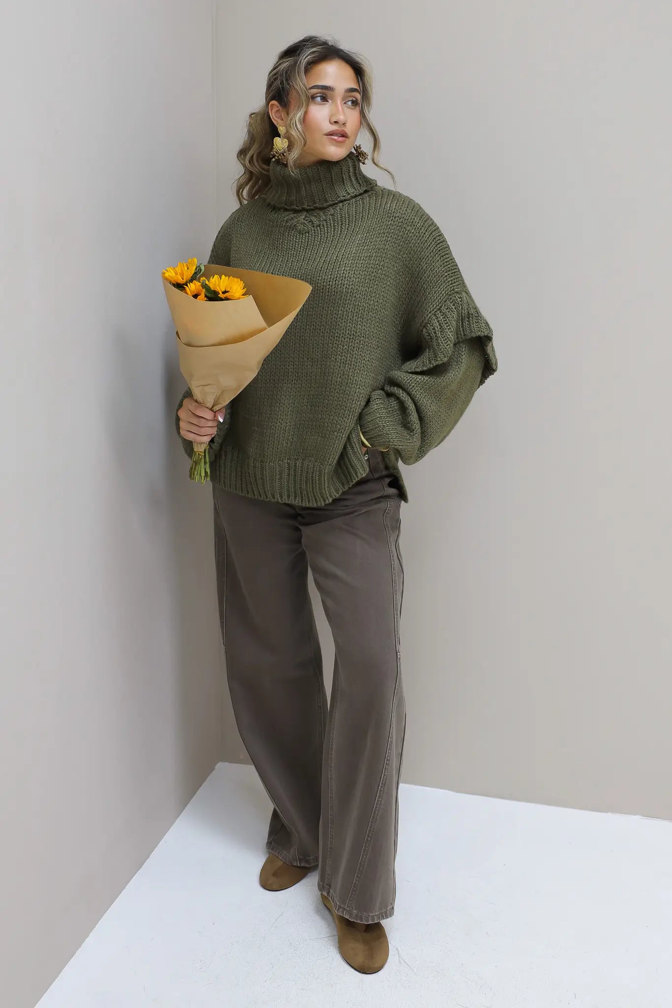 Model poseert recht vooruit met groene trui en bloemen