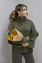 Model staat in studio met groene trui en donkerbruine broek