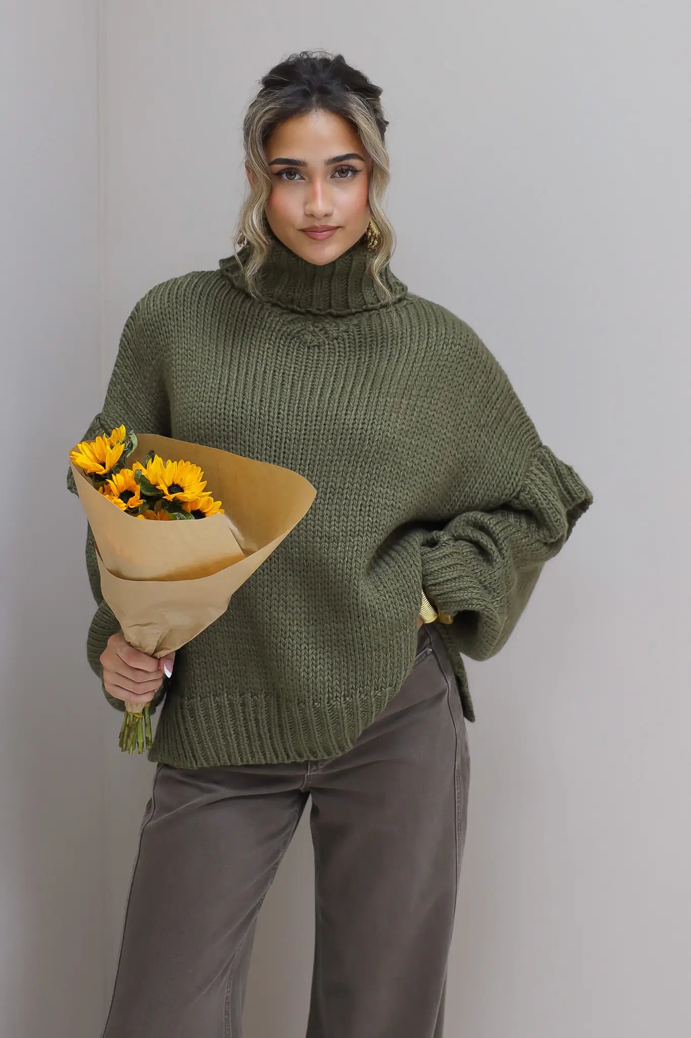 Model staat schuin gedraaid met groene trui