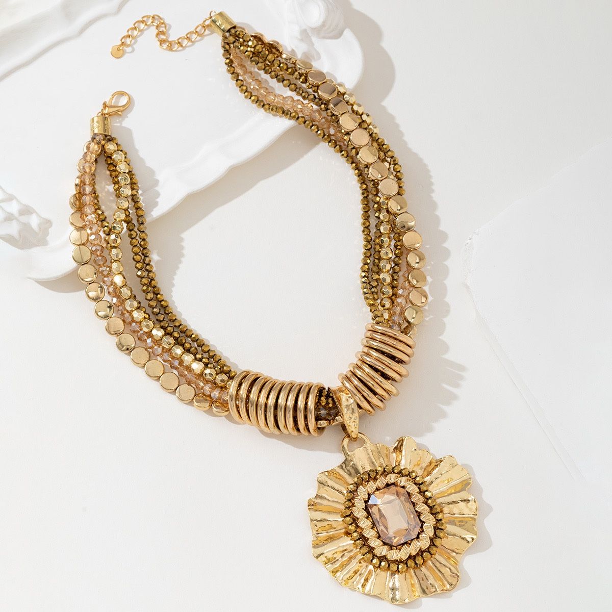 Grove gouden ketting met verschillende schakels en kralen en een grote ronde hanger schuin gefotografeerd