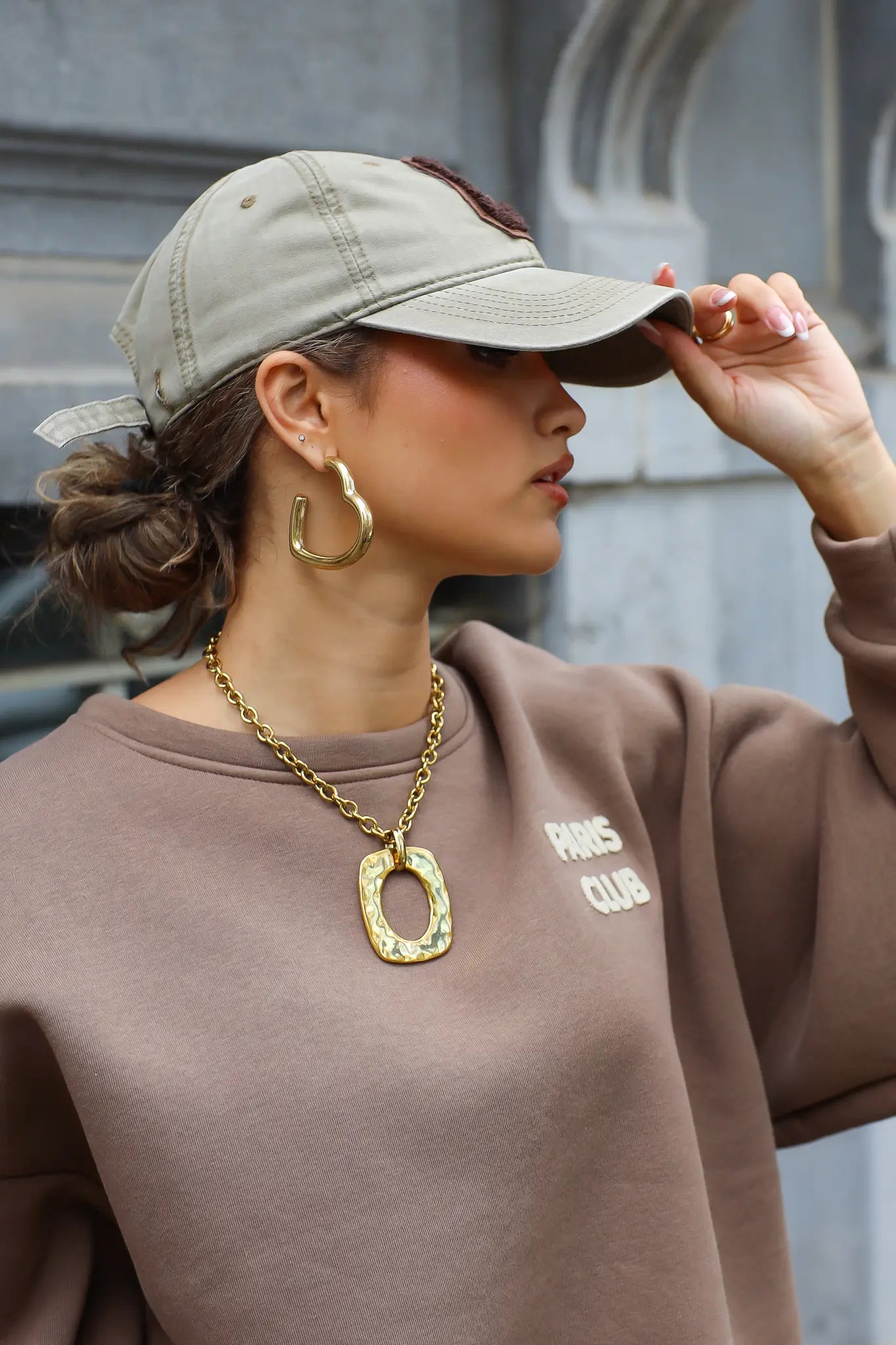 vrouw met beige honkbalpet met bruine letter c en goudkleurige ketting close up gefotografeerd