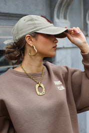 vrouw met beige honkbalpet met bruine letter c en goudkleurige ketting close up gefotografeerd