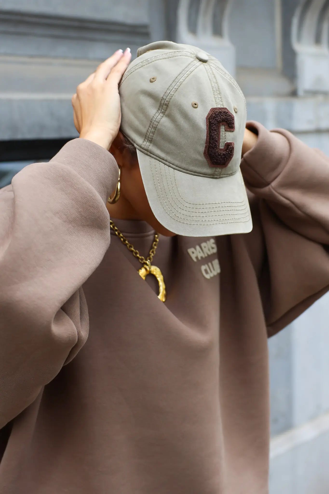 vrouw met beige honkbalpet met bruine letter c en beige trui met paris club opdruk