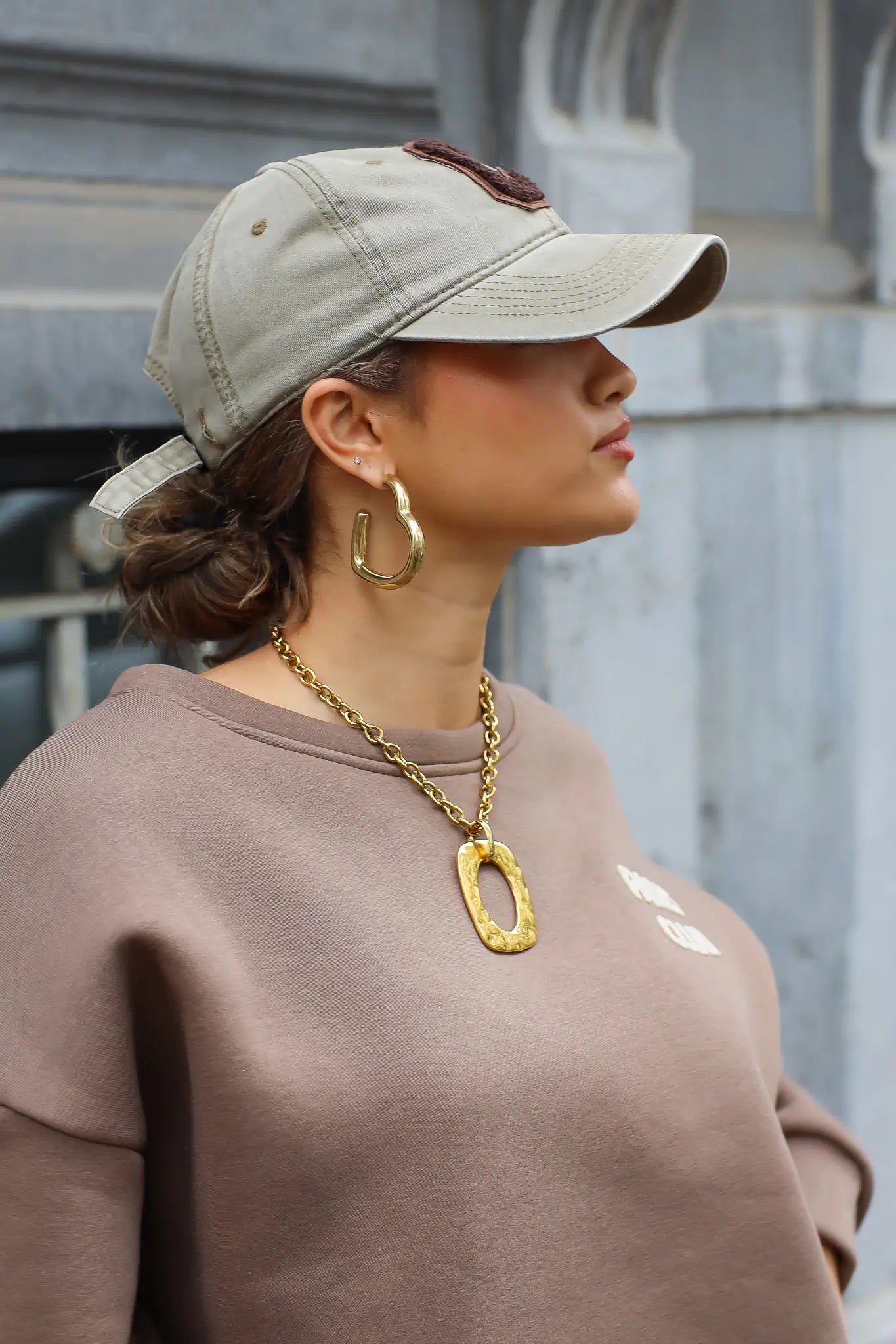 zijaanzicht van vrouw met beige honkbalpet met bruine letter c en beige trui