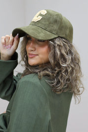 vrouw met krullen draagt groene honkbalpet met beige letter c en groene jas