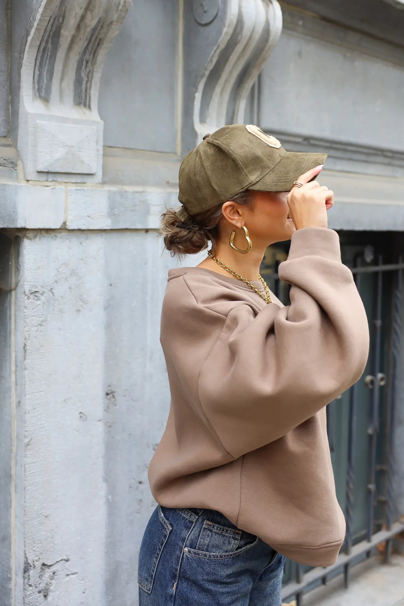 vrouw met beige trui en groene honkbalpet met beige letter c van achteren gefotografeerd