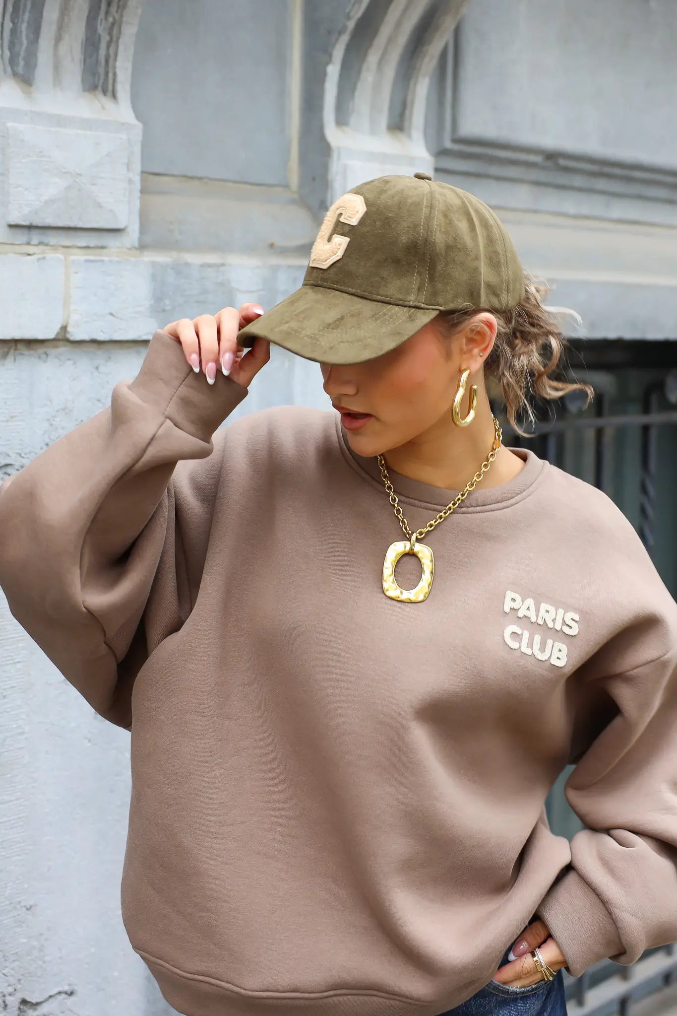 vrouw met groene honkbalpet met beige letter c en beige trui met opdruk paris club